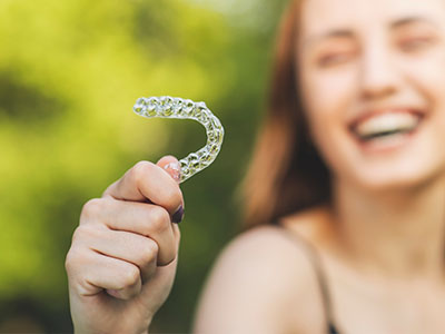 The image shows a person holding up a toothbrush with braces attached, smiling at the camera.